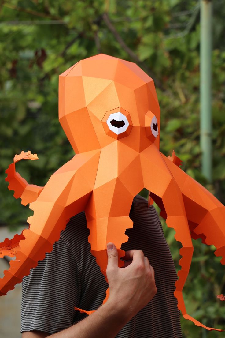 an orange origami octopus mask being held by a man