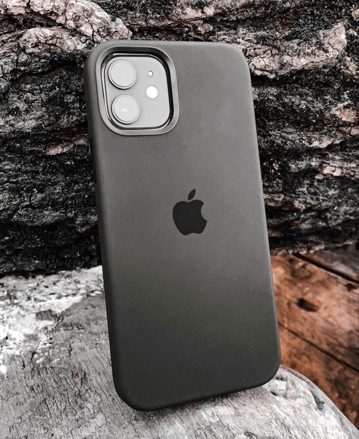 an iphone case sitting on top of a rock next to a tree trunk and stone wall