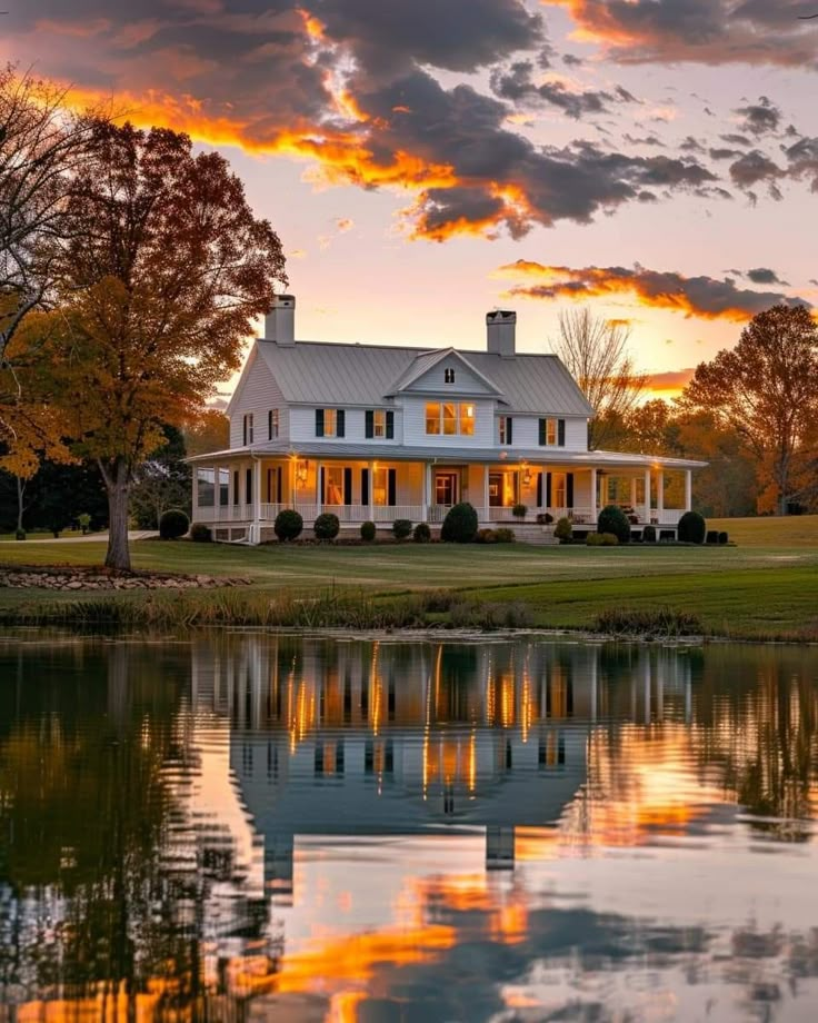 a large white house sitting on top of a lush green field next to a lake