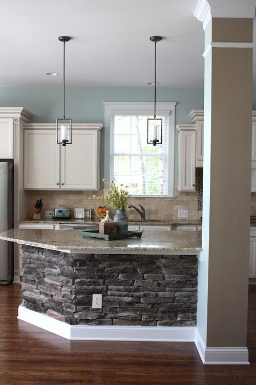 a kitchen with an island made out of stone and wood flooring, along with white cabinets