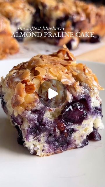 a piece of blueberry almond pralie cake on a plate with the rest of it in the background