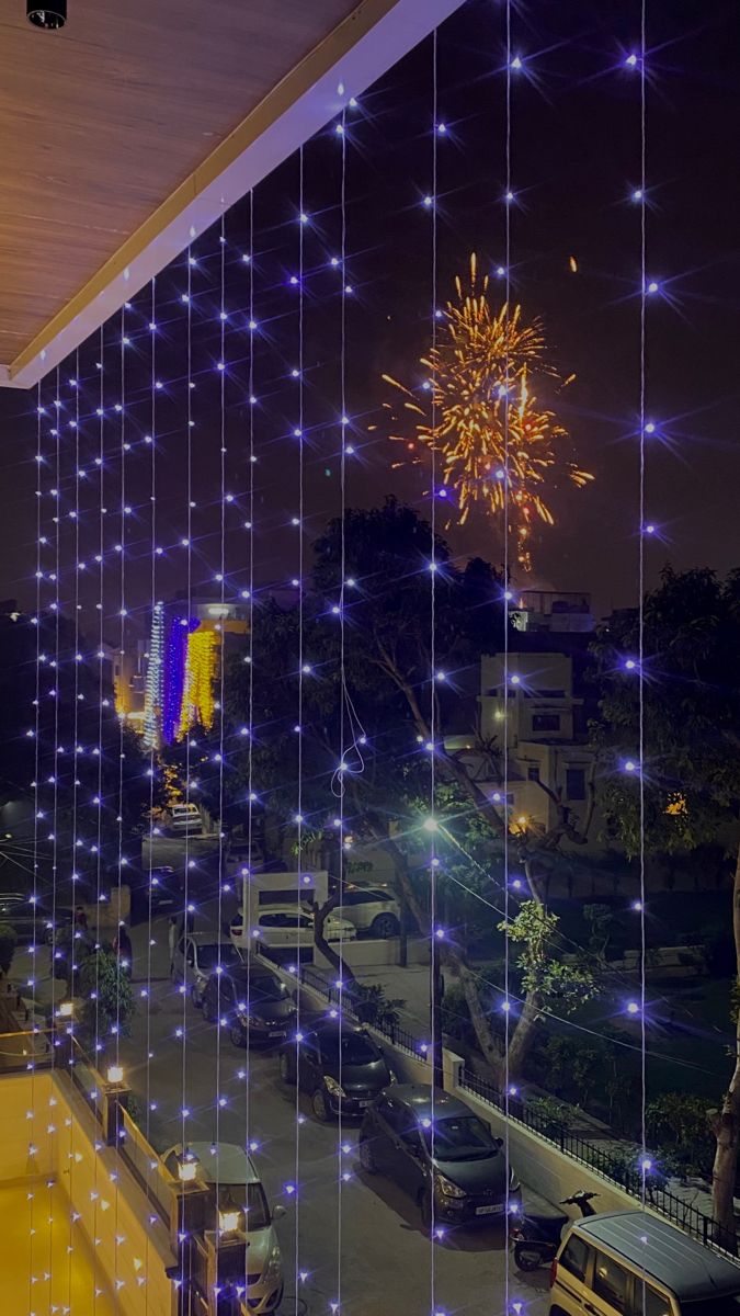 fireworks are lit up in the night sky over a city street with parked cars and buildings