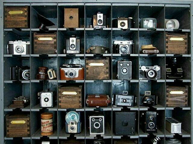 an assortment of old cameras on display in a metal shelf with wooden crates and bins