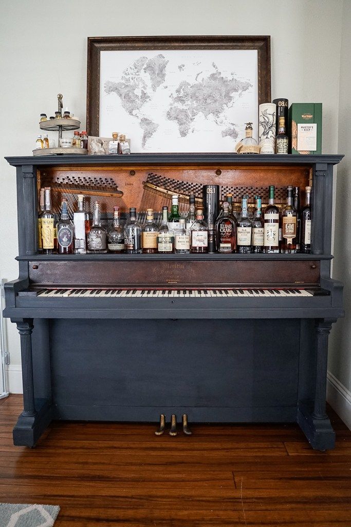 an old piano with liquor bottles on it and a world map above the top shelf