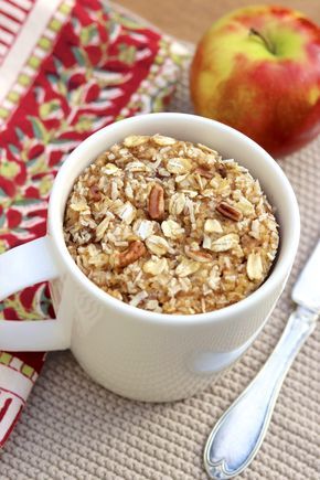 a bowl of oatmeal next to an apple on a place mat with spoons