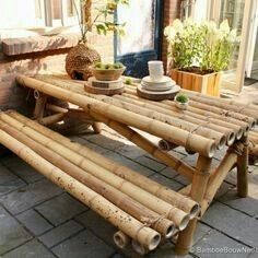 a table made out of bamboo sticks on a brick patio with potted plants in the background