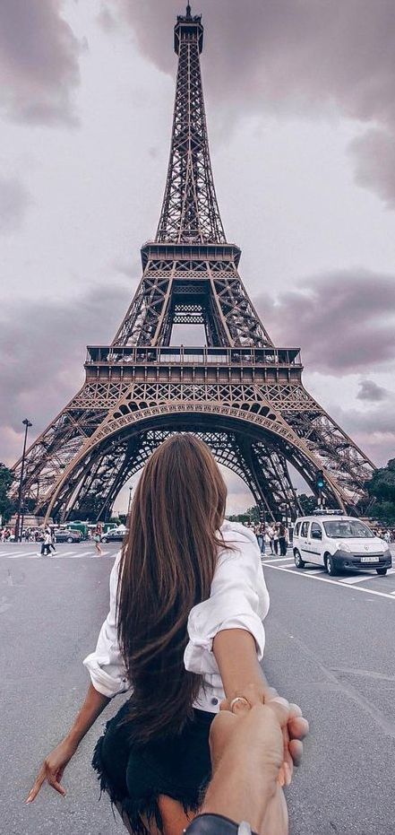 a woman holding the hand of a man in front of the eiffel tower