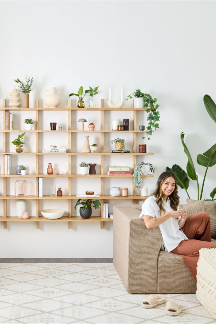 a woman sitting on a couch in front of a shelf with plants and potted plants