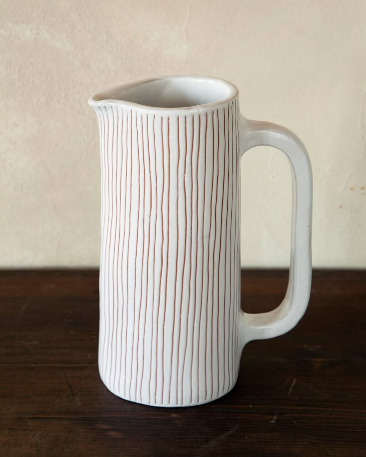 a white and red striped mug sitting on top of a wooden table next to a wall