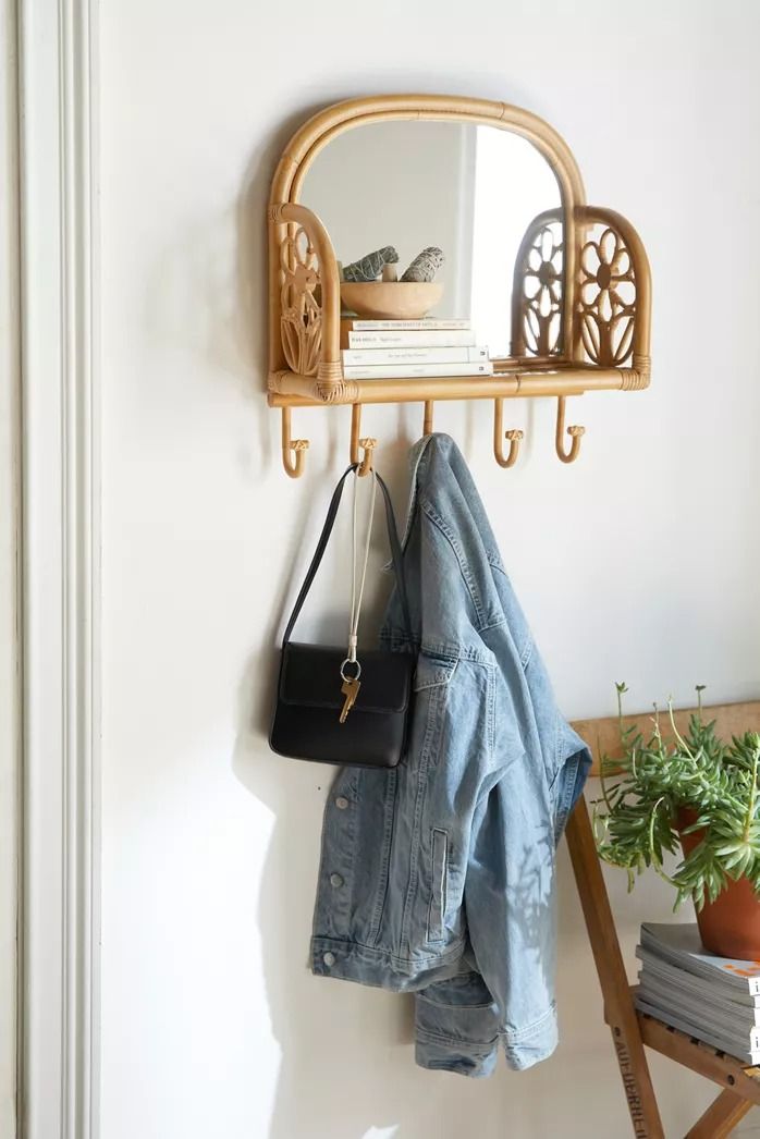 a mirror and coat rack on a white wall next to a wooden ladder with a black purse