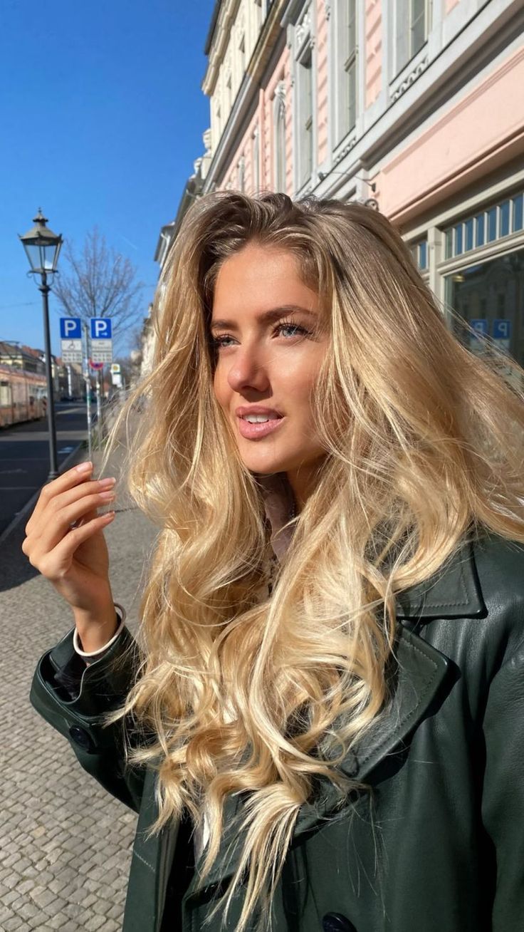 a woman with long blonde hair standing in front of a street sign and looking at the camera