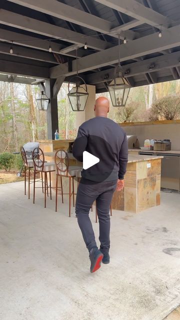 a man is running in front of an outdoor kitchen and dining room area with chairs