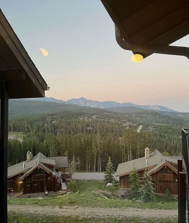 the view from inside a cabin looking out at mountains and trees in the distance with lights on