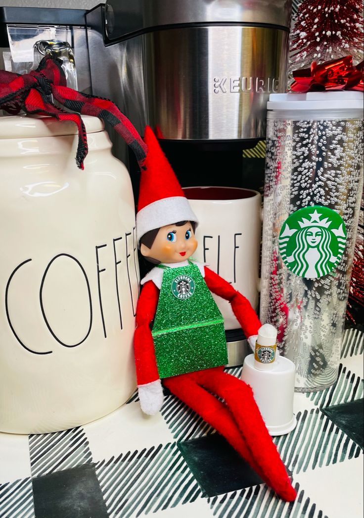 an elf is sitting on the counter next to starbucks mugs and other holiday decorations