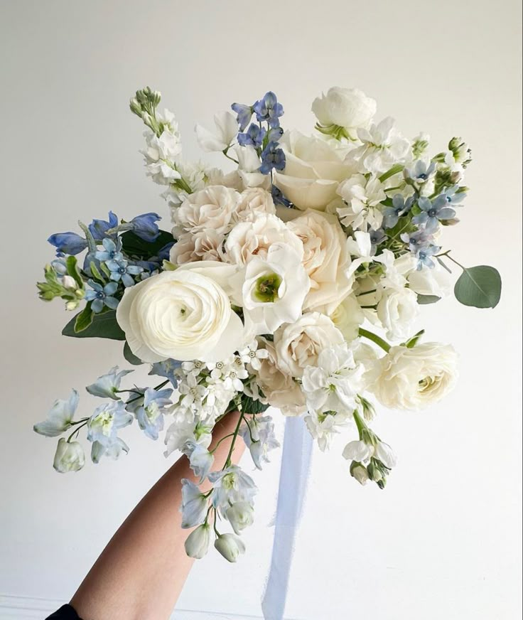 a bouquet of white and blue flowers in someone's hand