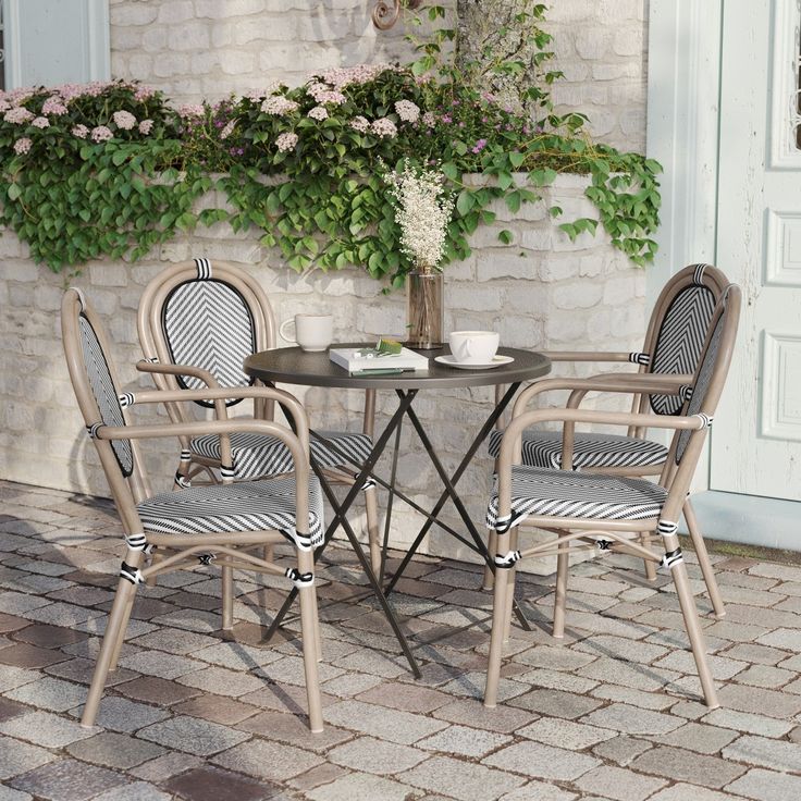 the table and chairs are outside by the wall with flowers in vases on it