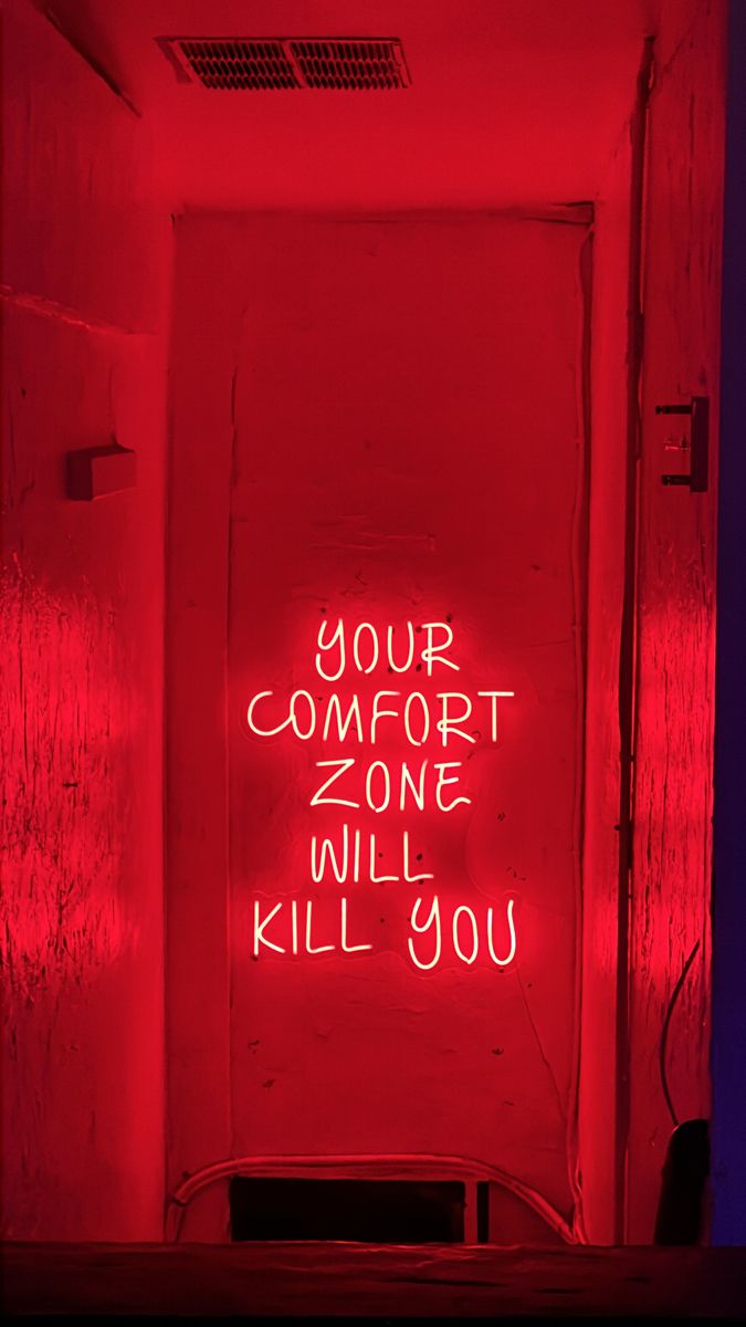 a neon sign that says your comfort zone will kill you on the wall behind it