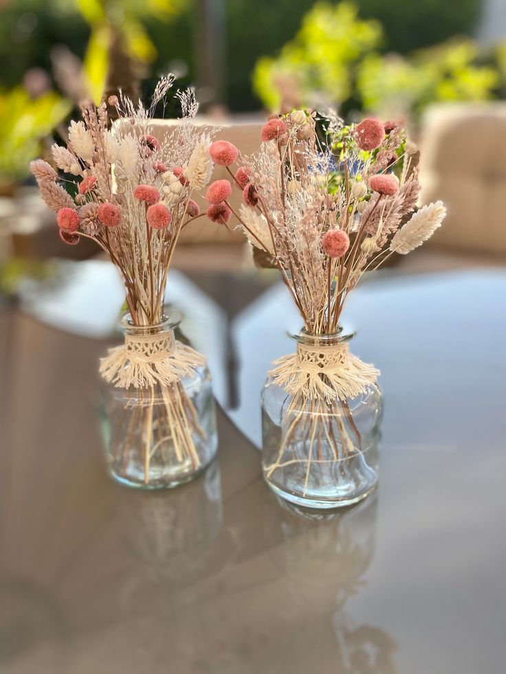 two glass vases with dried flowers in them on top of a dining room table