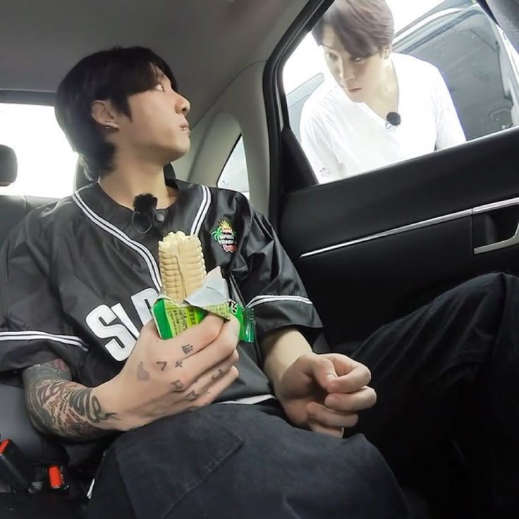 a young man sitting in the back seat of a car holding a sandwich and fries