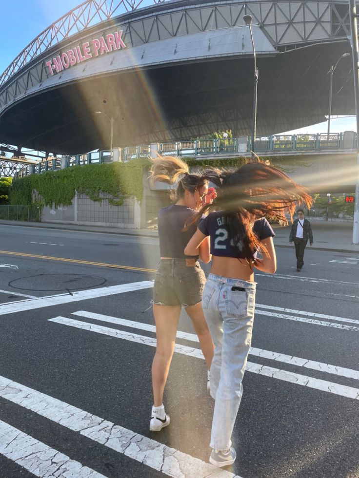 two girls walking across the street in front of a stadium