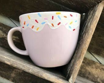 a pink cup with sprinkles on it sitting on top of a wooden shelf