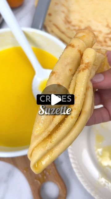 crepes are being held in front of a bowl of orange juice and pancakes