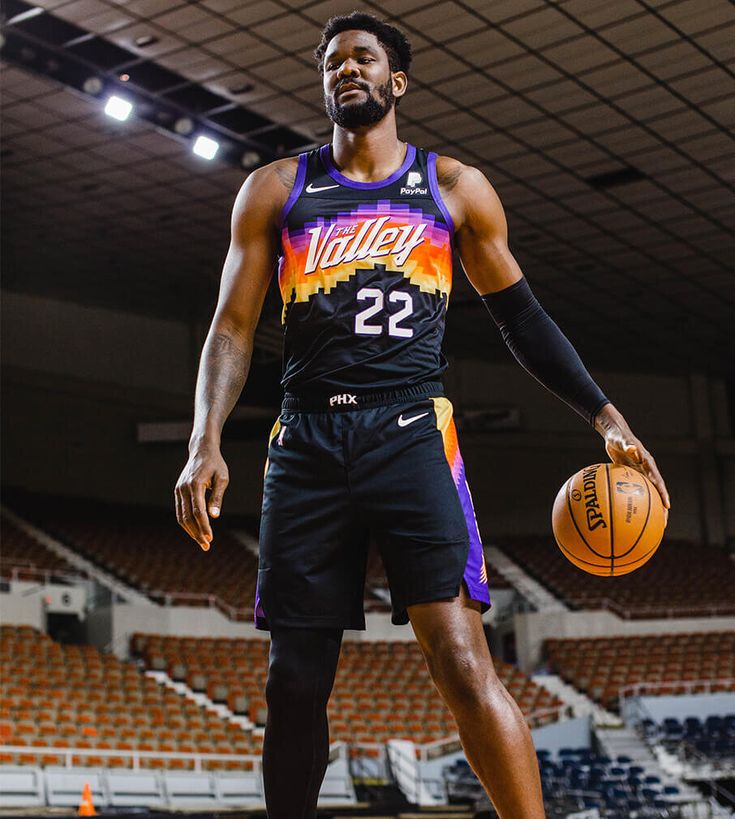 a man holding a basketball in his right hand and standing on a court with an empty bleachers behind him