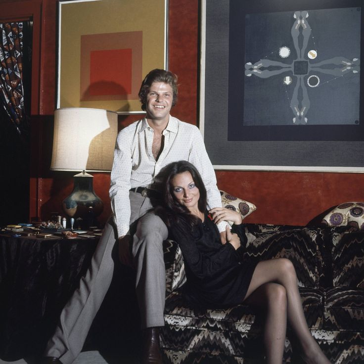 a man and woman sitting on a couch in front of a painting, posing for the camera