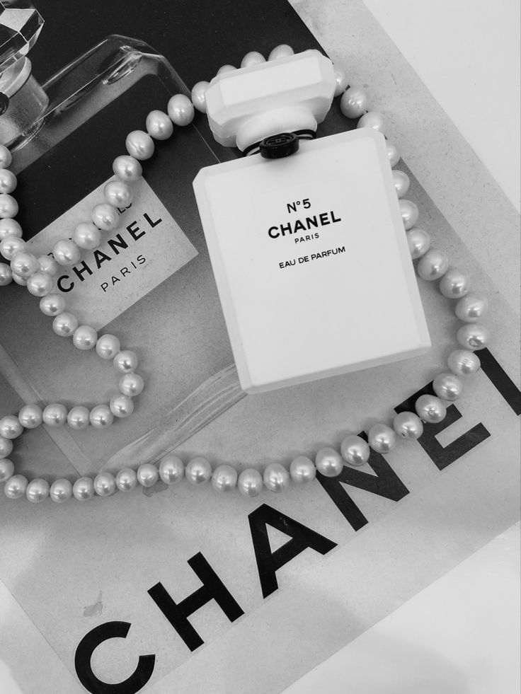 a chanel perfume bottle and pearls necklace on top of a magazine with an advertise