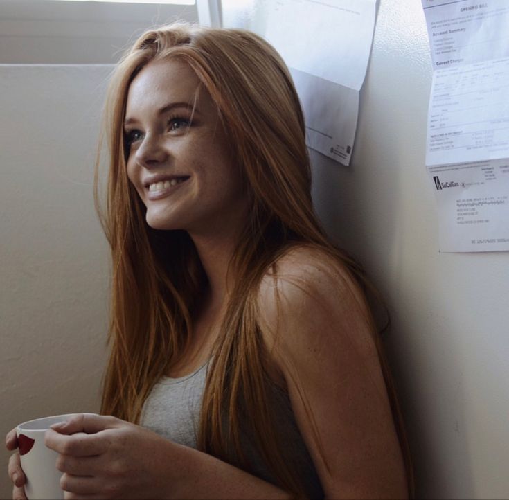 a woman leaning against a wall holding a coffee cup