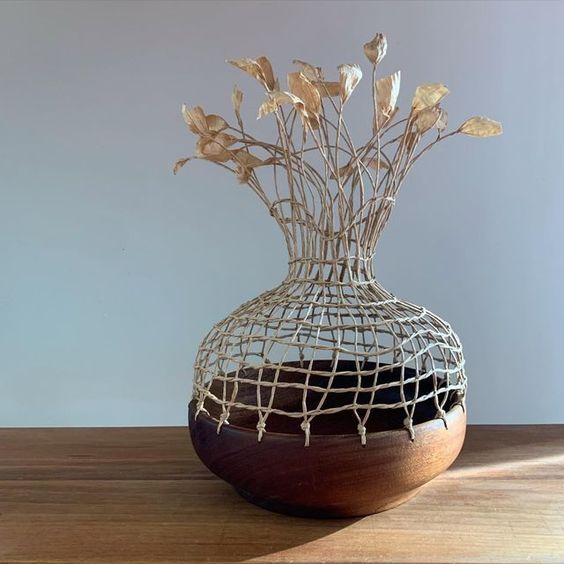 a vase that has some kind of wire wrapped around it with flowers in it on a wooden table