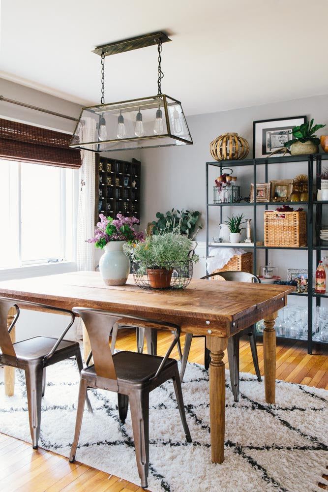 a dining room table and chairs with plants on the shelf behind it in front of a window