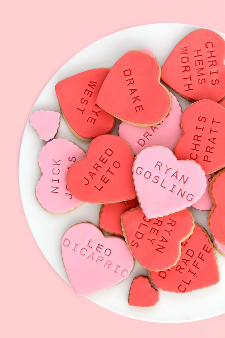 valentine's day cookies with names and hearts on a white plate against a pink background