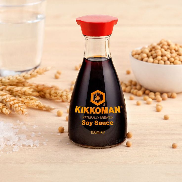 a bottle of soy sauce sitting on top of a wooden table next to some grains