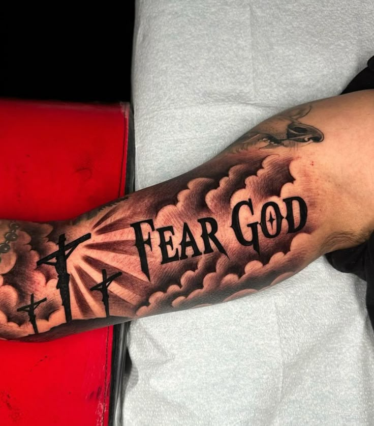 a man's arm with the words fear god on it and clouds in the background