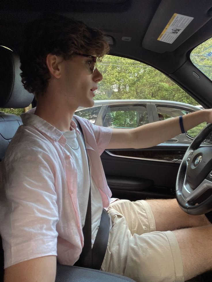 a man sitting in the driver's seat of a car with his hand on the steering wheel