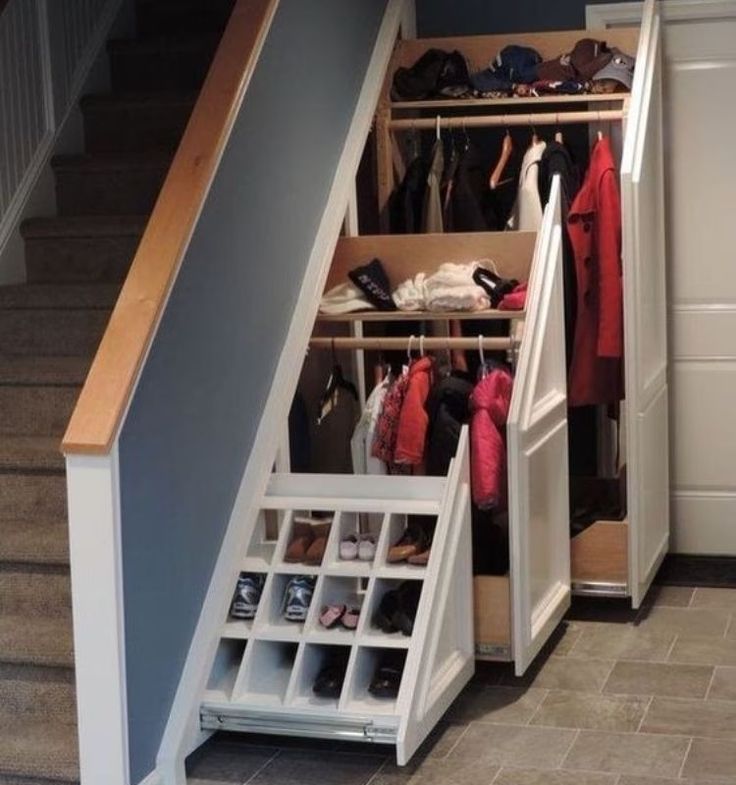 an open closet under stairs with shoes and coats