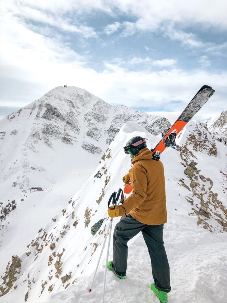 a man standing on top of a snow covered slope holding skis in his hand