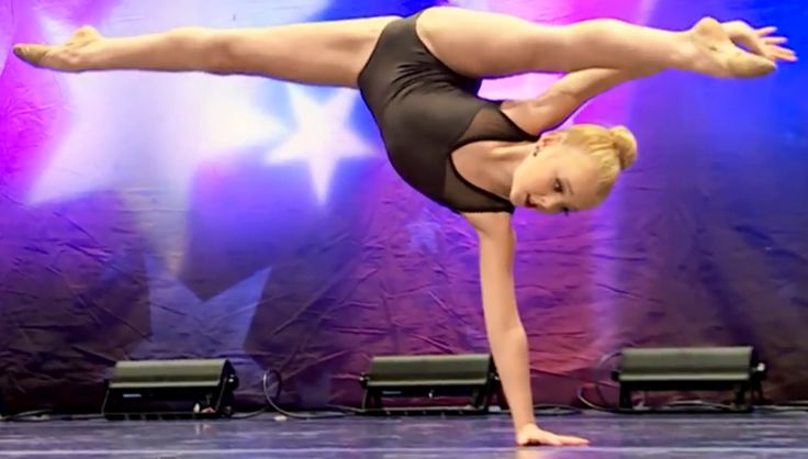 a woman in a black leotard doing a handstand on a stage