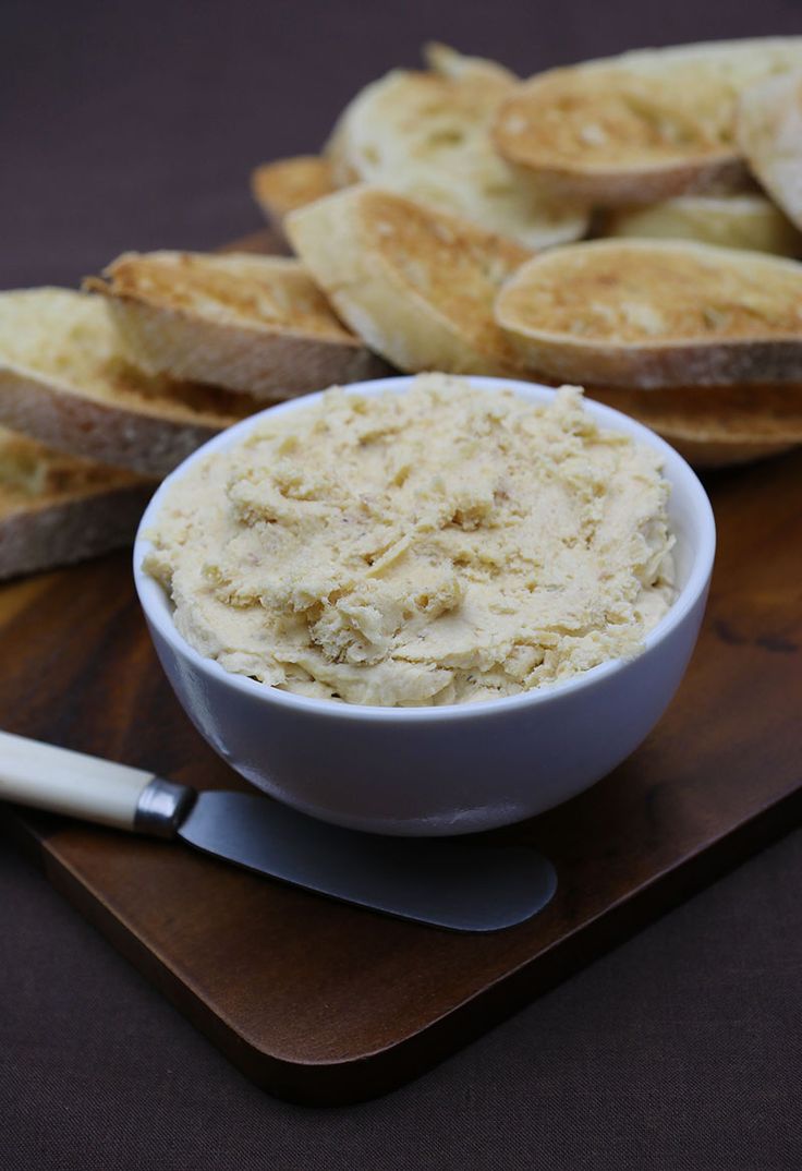 a bowl of dip next to slices of bread on a cutting board