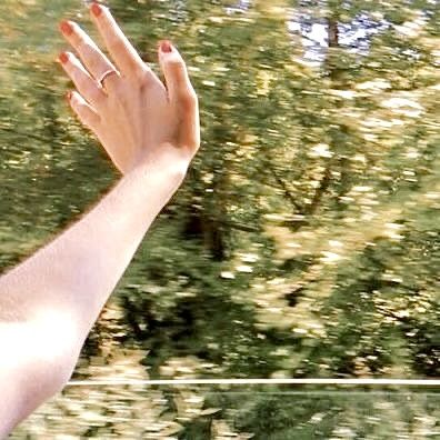 a person's hand reaching out the window of a car with trees in the background