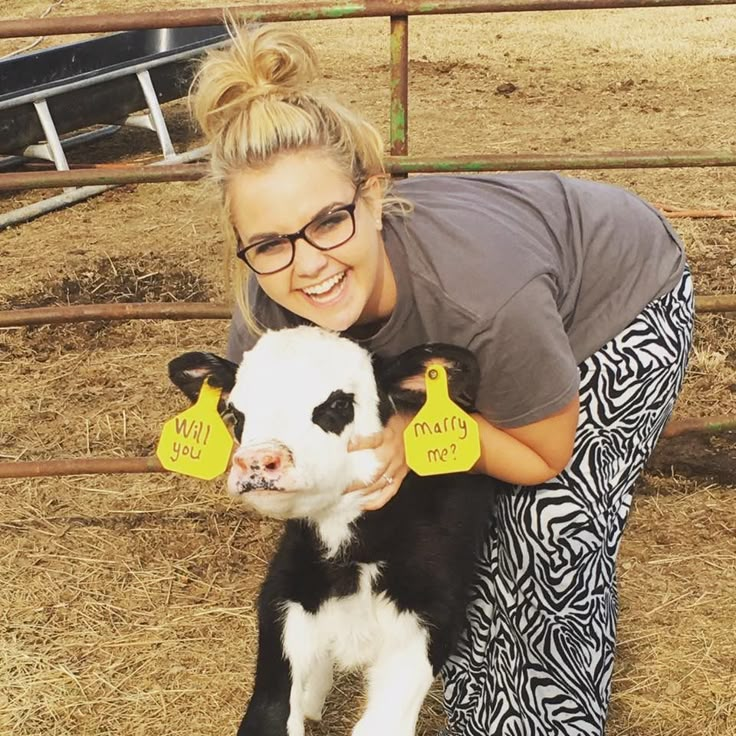 a woman holding a baby cow with tags on it's ears in front of a fence