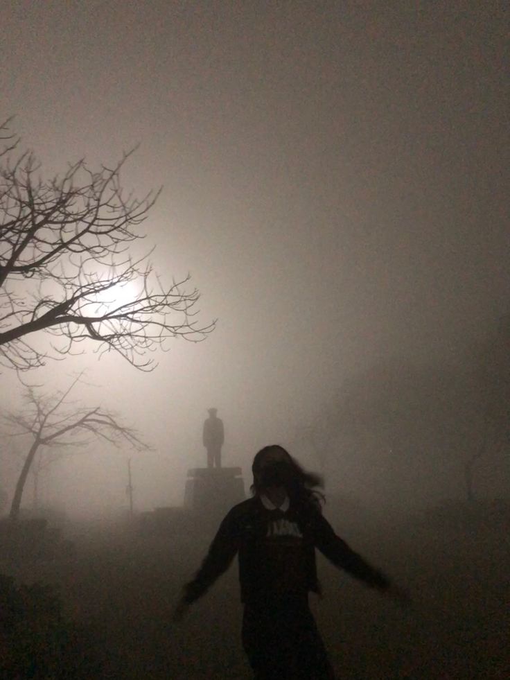 a person is walking in the fog with their arms out and there is a clock tower in the distance