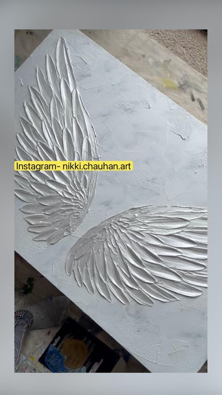 an artistic painting with white paint and wings on the side of a piece of metal