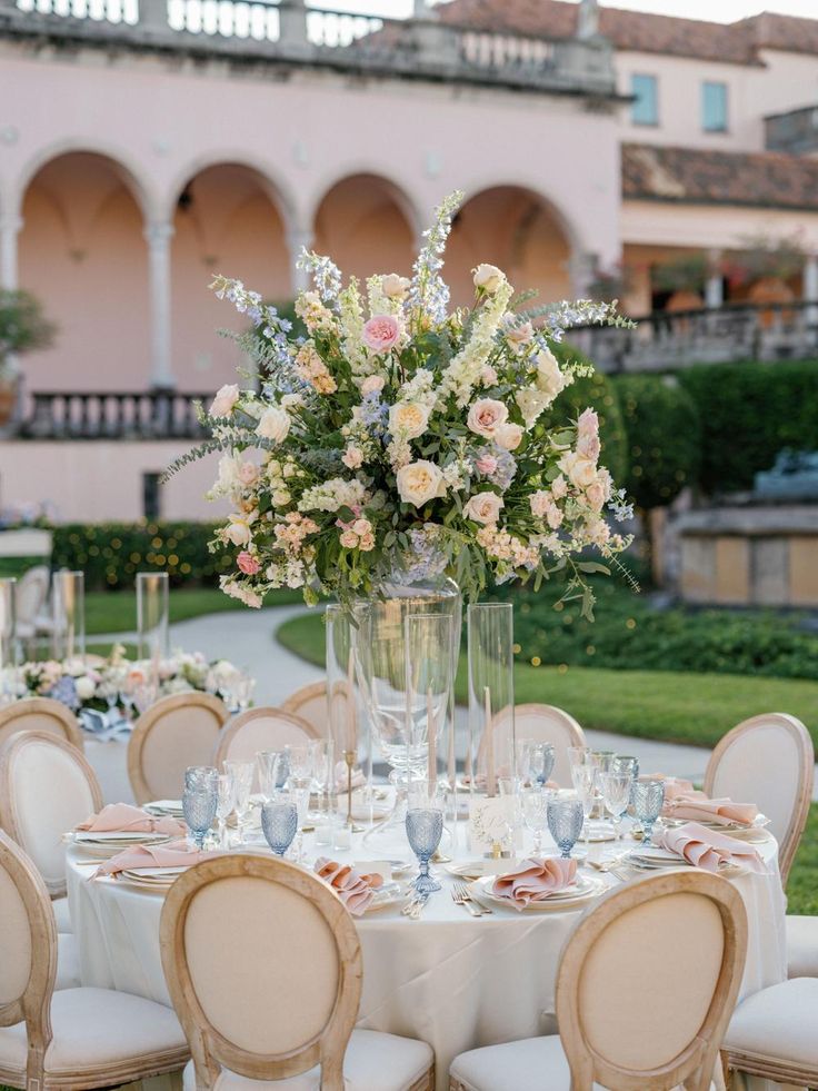 a table set up for a formal dinner with flowers in a vase on the center