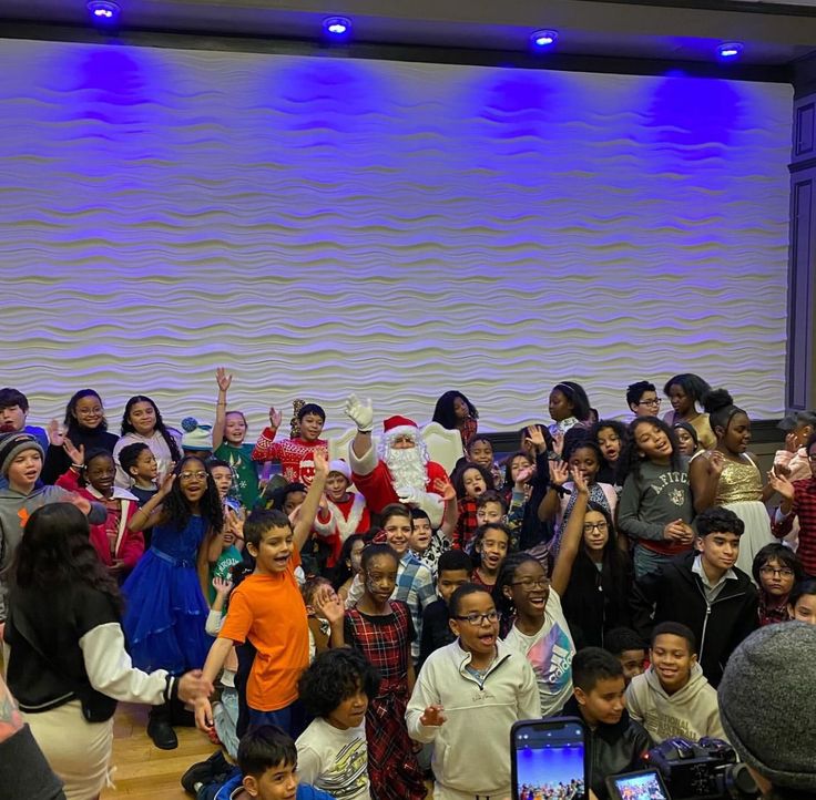 a group of people standing around each other in front of a screen with santa clause on it