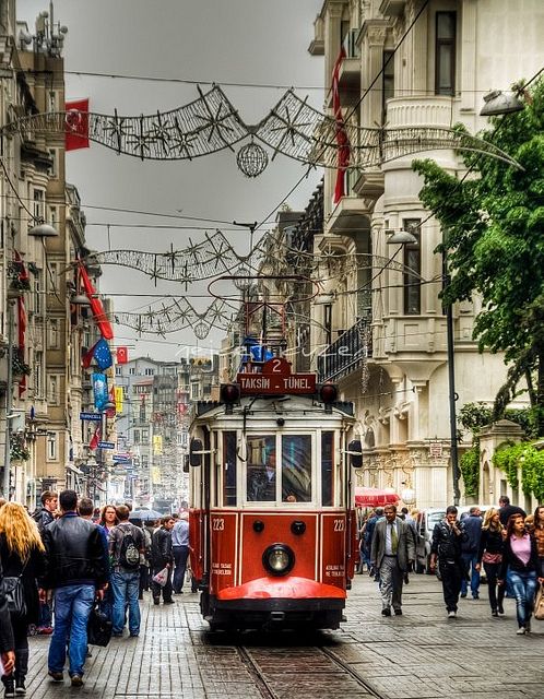 a red trolley car traveling down a street next to tall buildings with lots of people