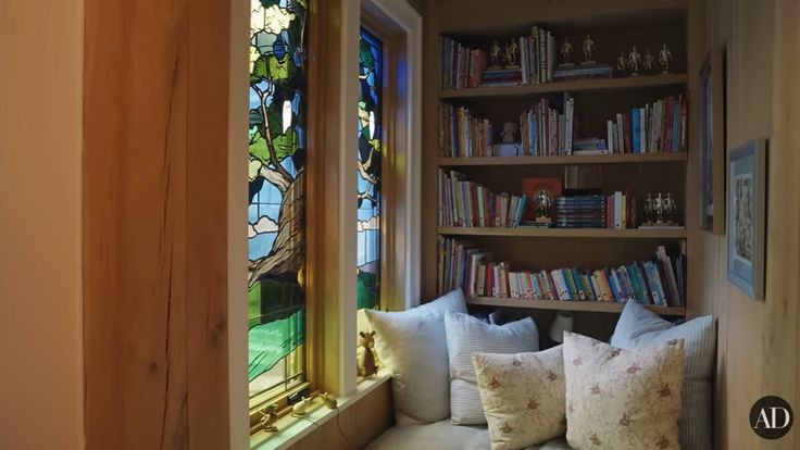 a window seat in front of a book shelf with books on it and two pillows