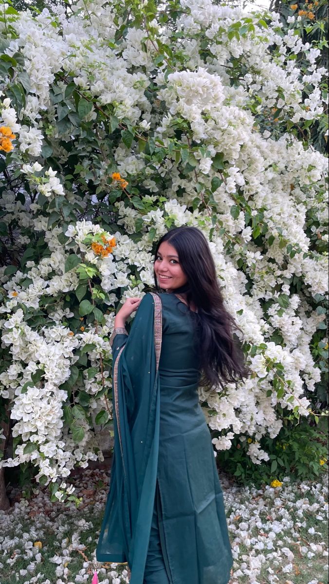 a woman standing in front of white flowers wearing a green dress and shawl over her shoulders