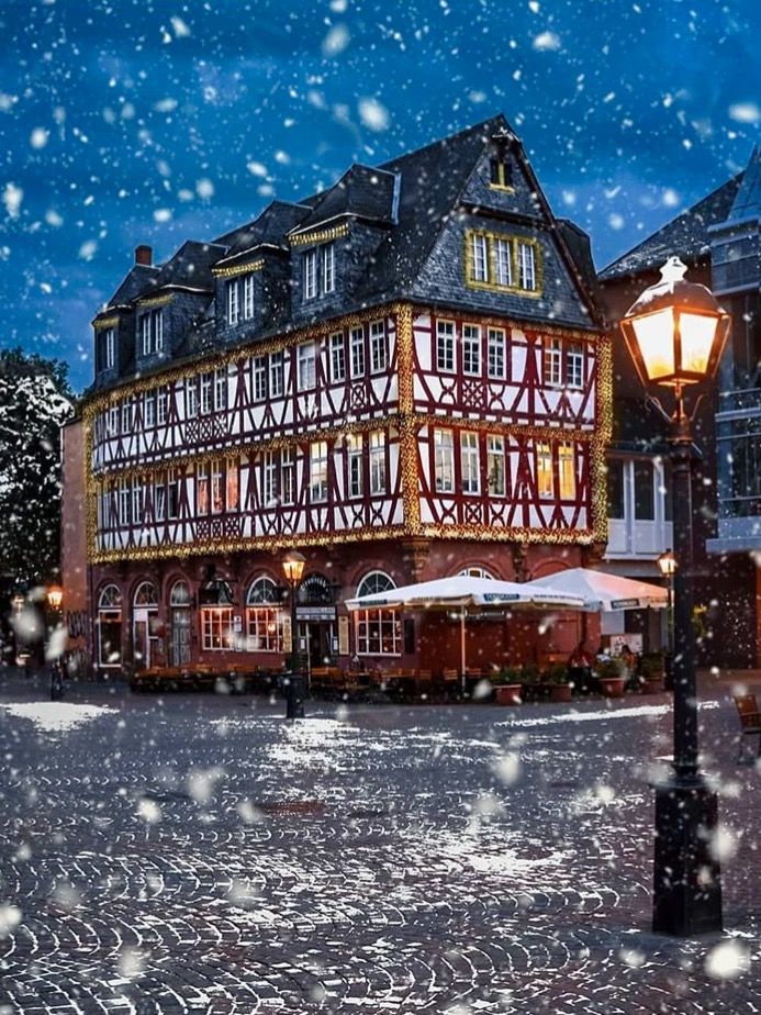 an old building with snow falling on the ground and street lights in front of it